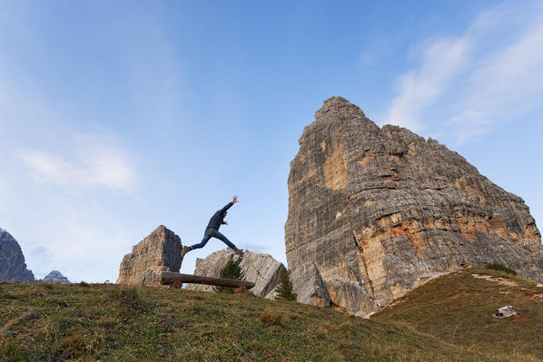 A hiker jumps in fornt of Cinque Torri, Dolomites, Cortina d'Ampezzo, Belluno province, Veneto, Italy