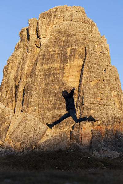 A hiker jumps in fornt of Cinque Torri, Dolomites, Cortina d'Ampezzo, Belluno province, Veneto, Italy