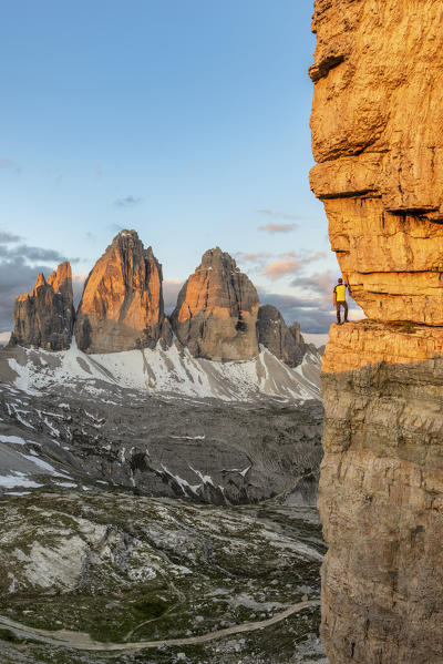 Sesto / Sexten, province of Bolzano, Dolomites, South Tyrol, Italy. A mountaineer admires the panorama from an exposed ledge at sunrise (MR)