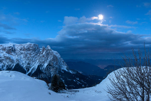 Alpe di Siusi/Seiser Alm, Dolomites, South Tyrol, Italy. Blue hour on  the plateau of Bullaccia/Puflatsch. In the background the peaks of Sciliar/Schlern and the lights of Bolzano City