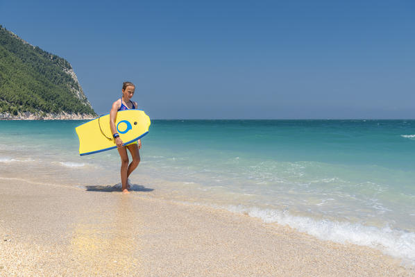 Sirolo, province of Ancona, Marche, Italy, Europe. A girl with a surfboard on the San Michele beach