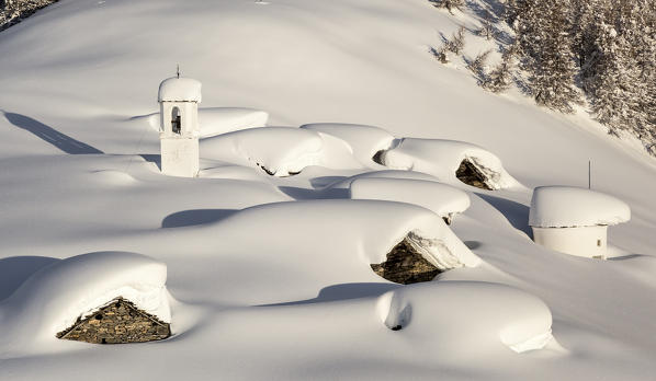 Italy, Italian Alps, Lombardy, The huts and the bell tower of Alpe Cima sorrounded by metres of snow