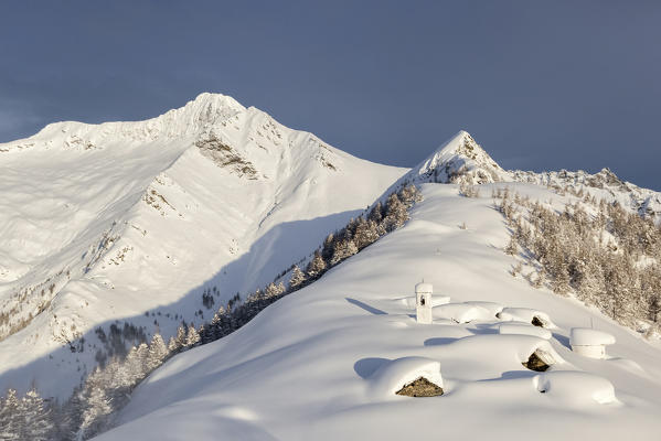 Italy, Italian Alps, Lombardy, The huts and the bell tower of Alpe Cima sorrounded by metres of snow