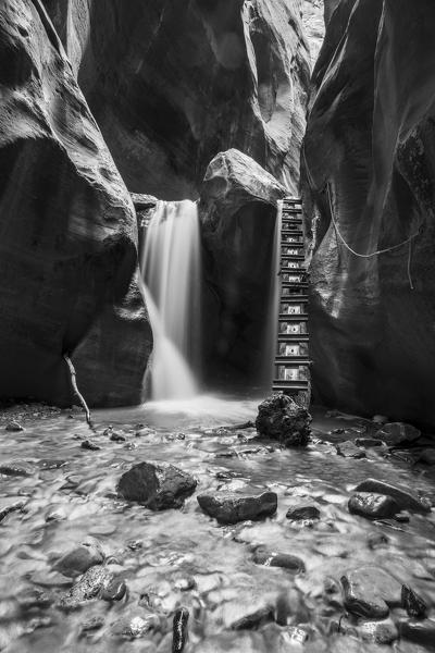 Black and white long exposure at waterfall and ladder in Kanarra Creek Canyon. Kanarraville, Iron County, Utah, USA.