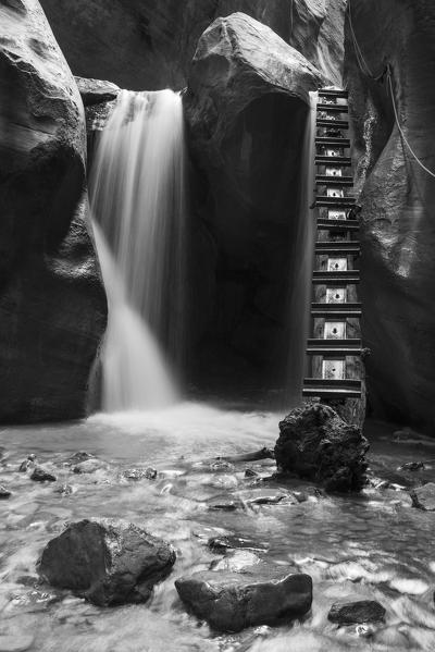 Black and white long exposure at waterfall and ladder in Kanarra Creek Canyon. Kanarraville, Iron County, Utah, USA.