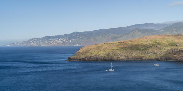 Boat sailing on the Atlantic Ocean at Point of St Lawrence, with the village of Canical in the background. Machico district, Madeira region, Portugal.