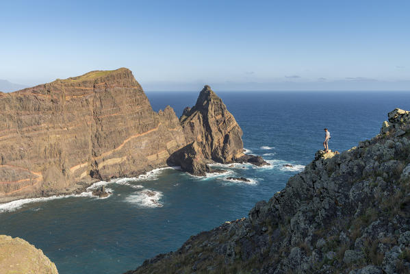 Man hiking at Point of St Lawrence, with Ponta do Castelo in the background. Canical, Machico district, Madeira region, Portugal.