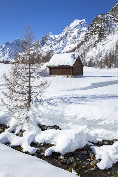 View of mountain huts near the torrent Devero in the small town of Crampiolo in winter. Alpe Devero, Antigorio valley, Piedmont, Italy.