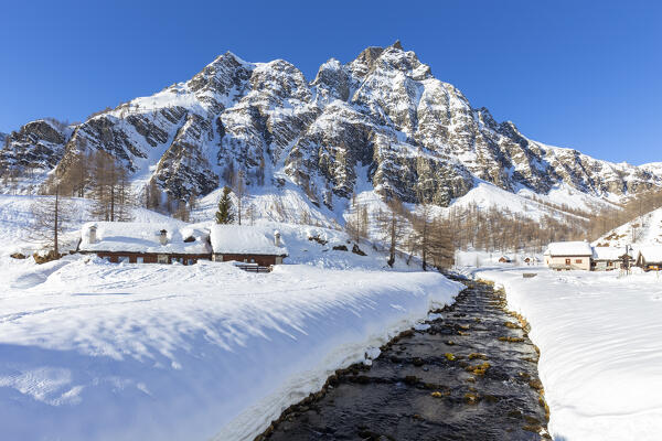 View of mountain huts near the torrent Devero in the small town of Crampiolo in winter. Alpe Devero, Antigorio valley, Piedmont, Italy.