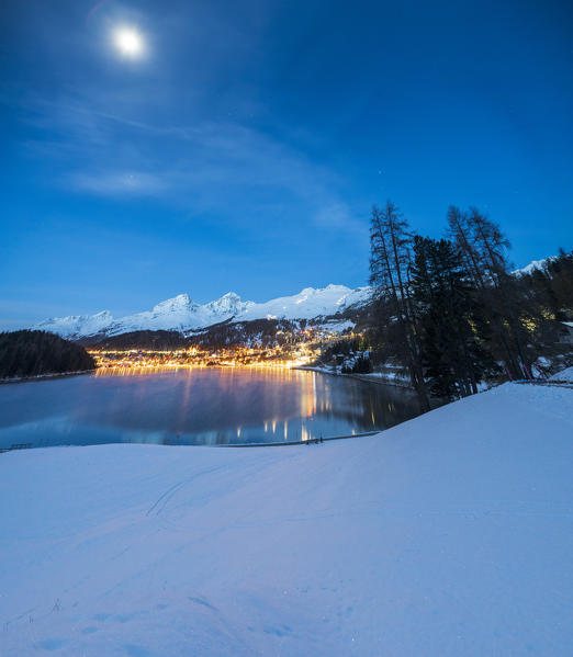 Panoramic of St Moritz and lake lit by moon during winter dusk, canton of Graubunden, Engadin, Switzerland