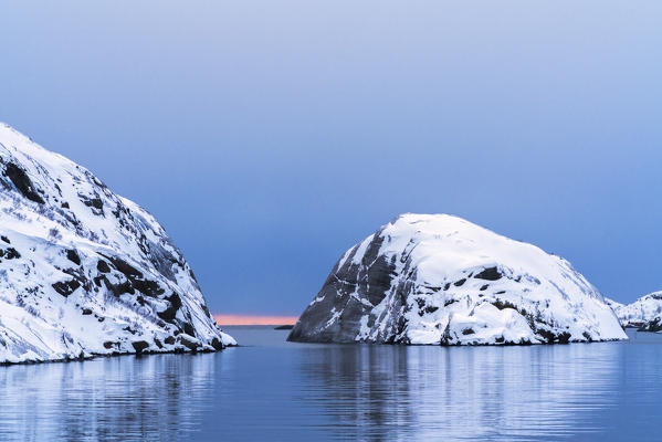 Dawn over snowy mountains and islets mirrored in the calm sea, Nusfjord, Flakstad, Lofoten Islands, Norway