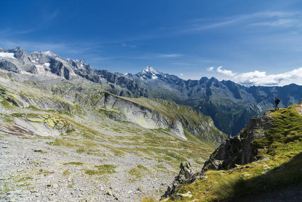 Hiker on rocks admiring Val Qualido from Passo Qualido in summer, Val Masino, Valtellina, Sondrio province, Lombardy, Italy