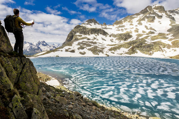 Hiker on rocks admiring Lej da la Tscheppa during spring thaw, St. Moritz, Engadin, canton of Graubunden, Switzerland