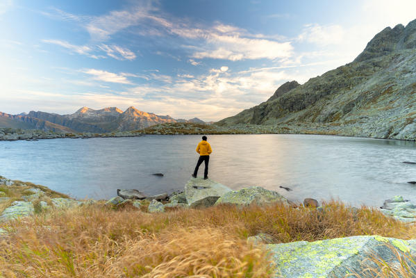 Rear view of man on rocks looking at Laghi Azzurri (Bergsee), Spluga Pass, Valle Spluga, Sondrio province, Valtellina, Lombardy, Italy