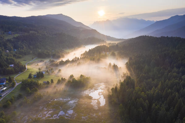 Misty sunrise above Pian di Gembro Nature Reserve, aerial view, Aprica, Sondrio province, Valtellina, Lombardy, Italy