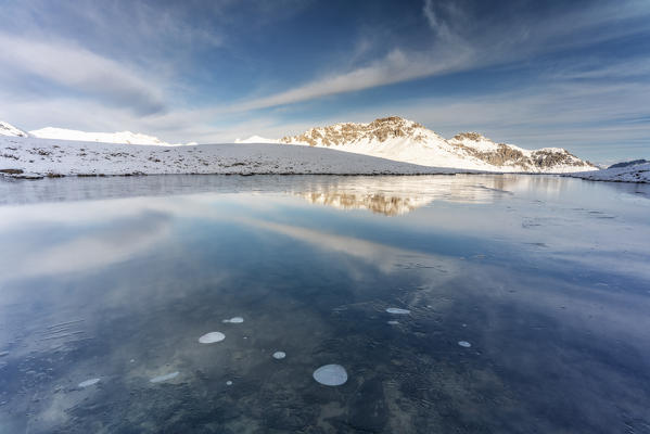 Piz Umbrail mirrored on icy surface of frozen lake, Braulio Valley, Stelvio Pass, Bormio, Sondrio province, Valtellina, Lombardy, Italy