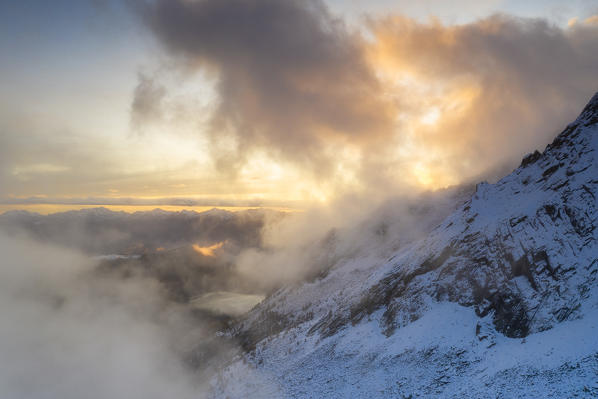 Foggy sky at sunset over mountains covered with snow, aerial view, Preda Rossa, Val Masino, Valtellina, Sondrio, Lombardy, Italy