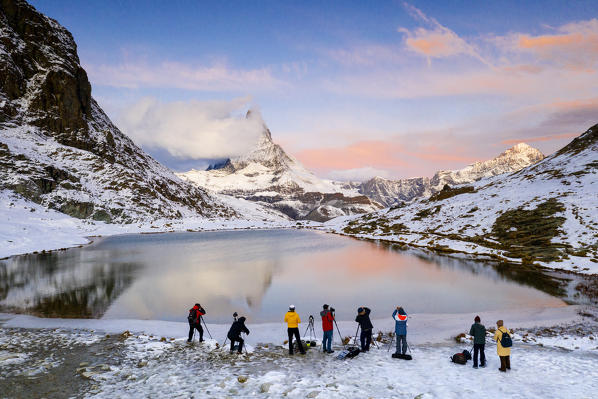 Group of photographers admiring Matterhorn from shores of icy Riffelsee lake at sunrise, Zermatt, canton of Valais, Switzerland