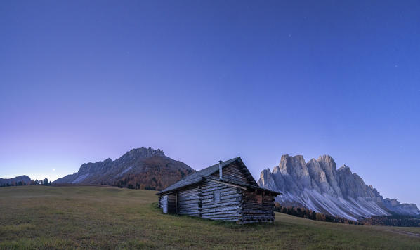 Panoramic of the autumn sunrise over the Odle and wood hut at Gampen Alm, Funes Valley, Dolomites, Bolzano, South Tyrol, Italy