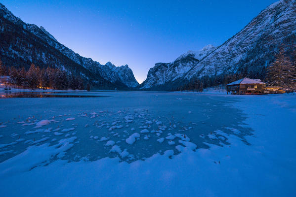 Blue dusk over lone chalet on shores of the icy Lake Dobbiaco, Val Pusteria, Dolomites, Bolzano province, South Tyrol, Italy