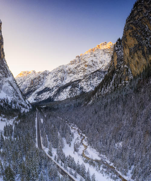 Sunrise on the Alemagna state road connecting Dobbiaco to Cortina along snowy woods, aerial view, Dolomites, South Tyrol, Italy