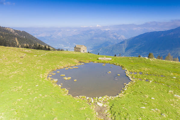 Stone hut in the green pastures of Motta di Olano in spring, Valgerola, Orobie Alps, Valtellina, Sondrio province, Lombardy, Italy