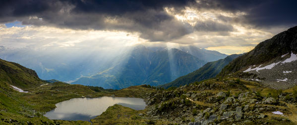 Sun rays during a backlight sunrise on mountain peaks surrounding Arcoglio lake, Valmalenco, Valtellina, Lombardy, Italy