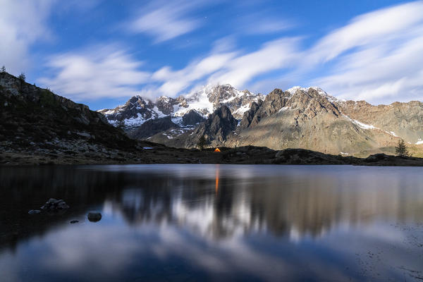 Isolated tent at feet of Monte Disgrazia mirrored in lake Zana at night, Valmalenco, Sondrio province, Valtellina, Lombardy, Italy