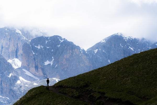 Foggy sky over a silhouette of man with hat walking on path around the Sassolungo group, Dolomites, Trentino-Alto Adige, Italy