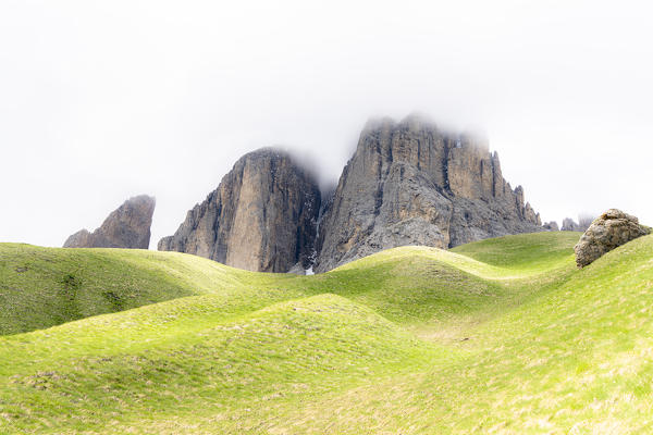 Fog over rocky peaks and green rolling landscape on trail around the Sassolungo group, Dolomites, Trentino-Alto Adige, Italy