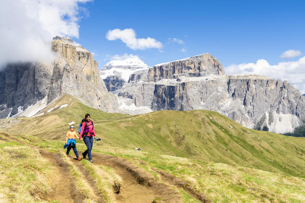 Mother and son smiling at camera on path with Sass Pordoi in background, Passo Sella, Dolomites, Trentino, Italy