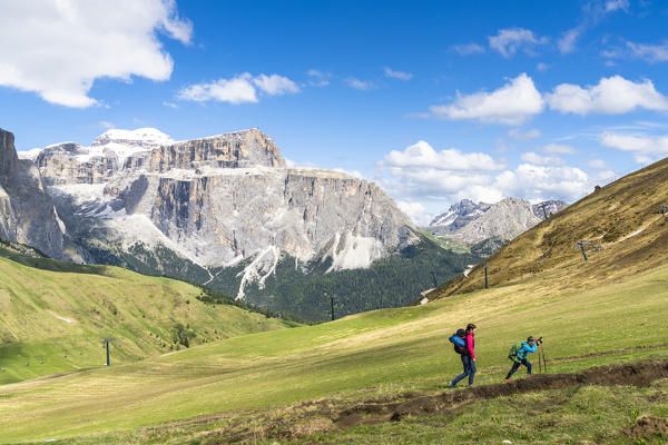 Mother and son on path along green meadows with Sass Pordoi in background, Passo Sella, Dolomites, Trentino, Italy