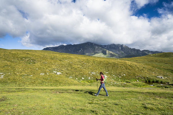 Side view of woman with hiking poles walking towards Pian dei Cavalli, Vallespluga, Valchiavenna, Valtellina, Lombardy, Italy