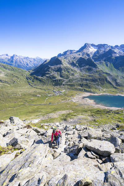 Hiker woman uphill on rocks towards Mount Cardine with lake Montespluga on background, Valchiavenna, Valtellina, Lombardy, Italy