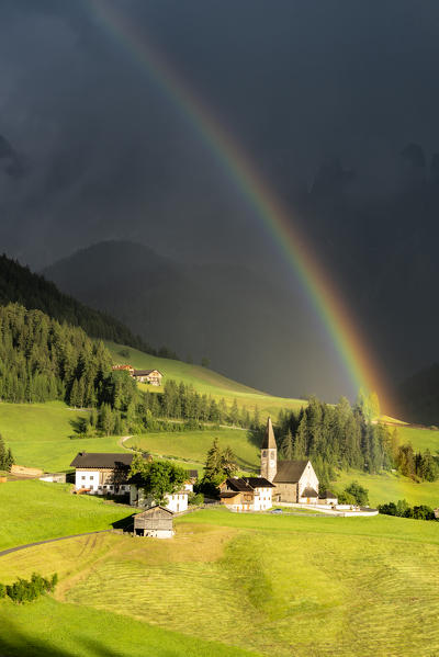 Bright rainbow in the dark sky over the village of Santa Magdalena, Val di Funes, Bolzano province, South Tyrol, Dolomites, Italy