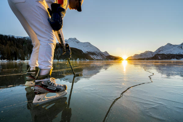 Portrait of man with ice skates and hockey stick on frozen Lake Sils at sunset, canton of Graubunden, Engadine, Switzerland (MR)