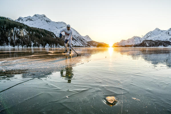 Young man playing ice hockey on frozen Lake Sils at sunset, canton of Graubunden, Engadine, Switzerland (MR)