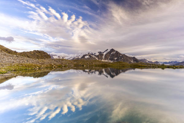 Fluffy clouds in the beauty sky at sunset over Tresero peak reflected in lake Manzina, Valfurva, Valtellina, Lombardy, Italy