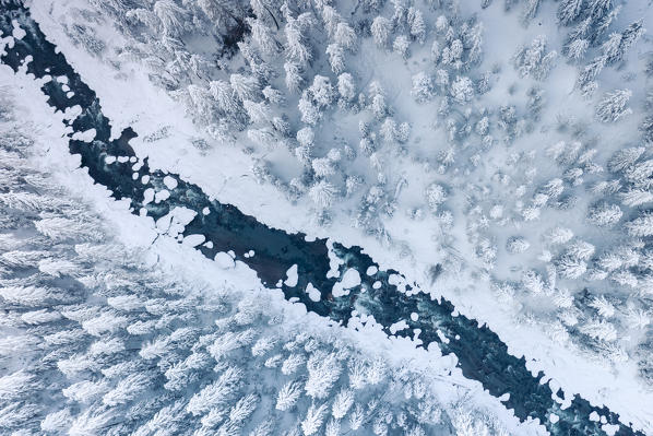 Aerial view of frozen river crossing the winter forest covered with snow, Switzerland