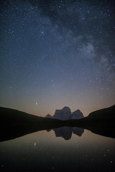 The milky way and Mount Pelmo reflected in the Lake of Baste in a clear summer night. Giau Pass, Cortina d'Ampezzo, Veneto Italy Europe