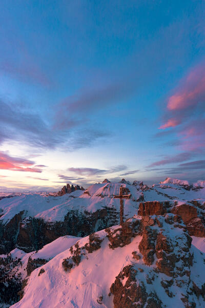 Sunset over the summit cross on Gran Cir mountain covered with snow and Odle peaks on background, Dolomites, South Tyrol, Italy