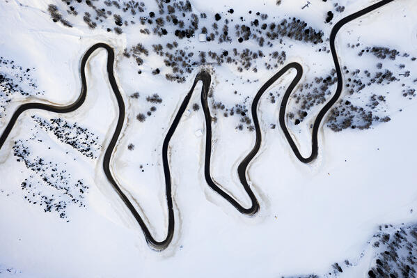 Narrow bends of icy road along the snow capped mountain pass from above, Dolomites, Italy