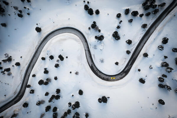 Mountain pass road crossing the winter forest covered with snow from above, aerial view, Dolomites, Italy