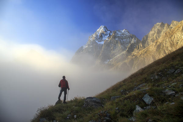 Hiker watching the clouds that rise from the valley and hide Monviso. Cozian Alps, Piedmont, Italy Europe