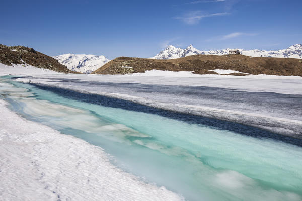 The crystal clear waters of Lake Emet are revealed to thaw. In the background the snow covered peaks. Madesimo. CHiavenna Valley. Spluga Valley. Valtellina. Lombardy. Italy. Europe