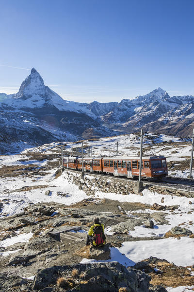 Hiker admires Matterhorn while white train of Gornergrat rides in the background. Zermatt, Canton of Valais, Switzerland Europe