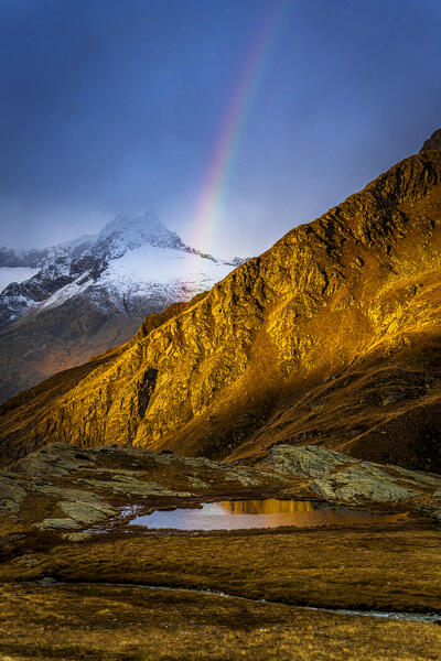 Colorful rainbow shining over majestic mountains in autumn, Alpe Fora, Valmalenco, Sondrio province, Lombardy, Italy