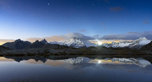 Hiker with head torch looking at the starry sky reflected in the alpine lake, Alpe Fora, Valmalenco, Valtellina, Lombardy, Italy