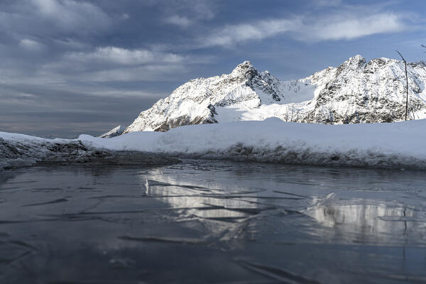 Monte Braccia and Cima Del Duca snowy mountains reflected in the frozen lake Entova, Valmalenco, Valtellina, Lombardy, Italy