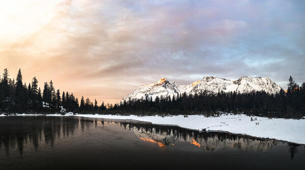 Snowy forest and mountains mirrored in lake Entova at sunrise, aerial view, Valmalenco, Valtellina, Lombardy, Italy